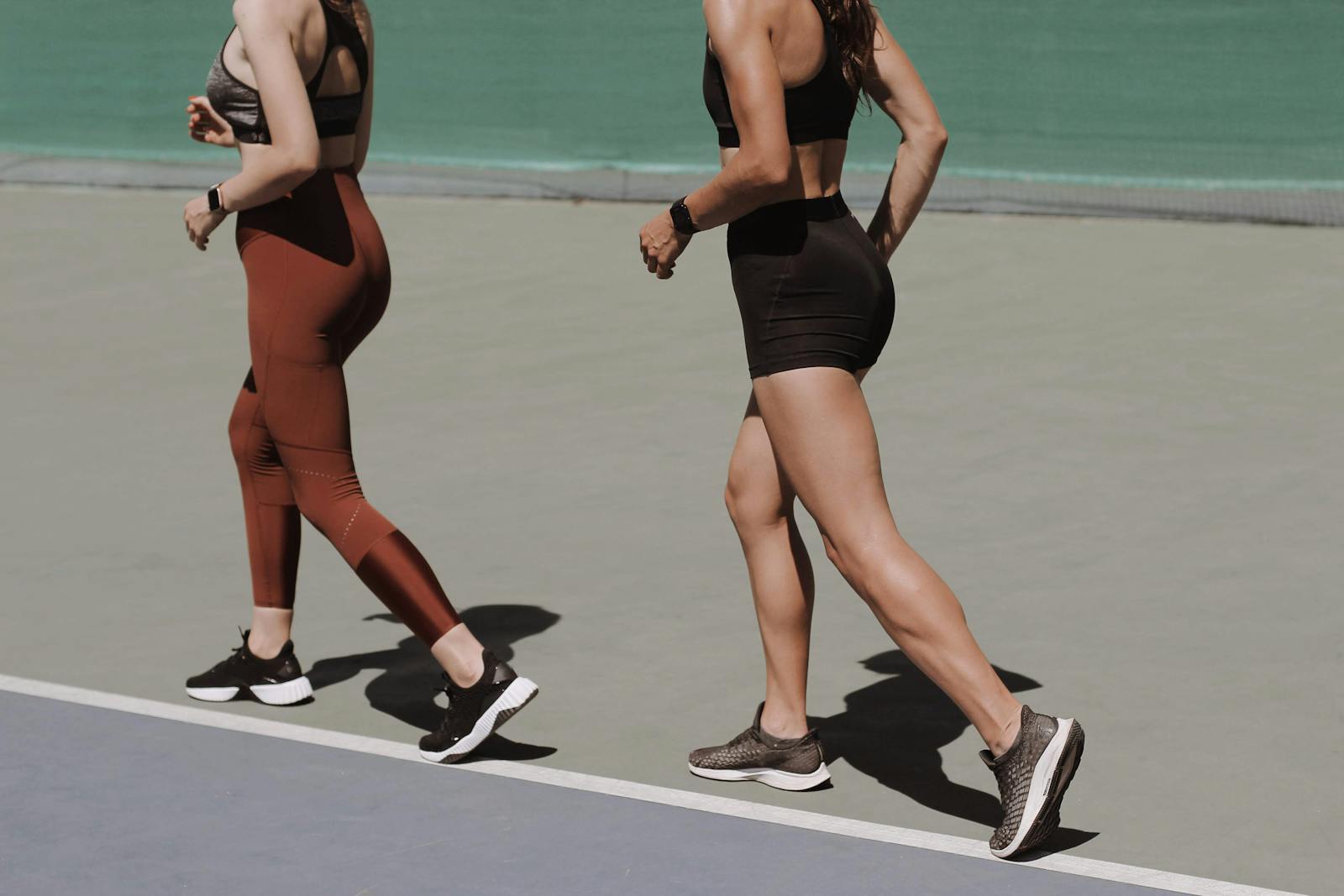 Two women walking on an outdoor track in sportswear, emphasizing healthy lifestyle and fitness.