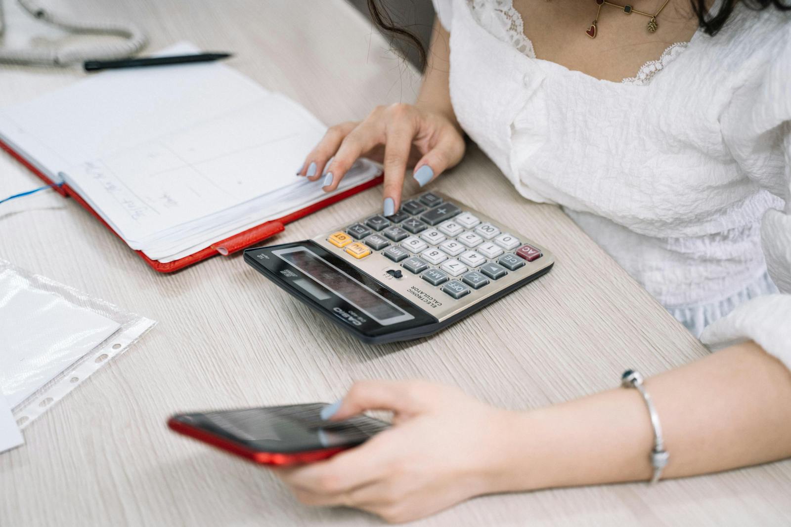 Close-up of a woman using a calculator and phone for budgetinh